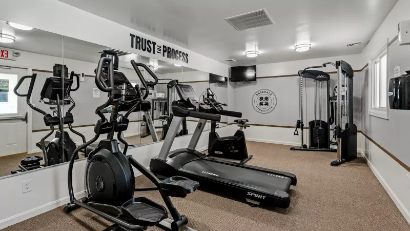Fully equipped fitness center at Rosedale Apartments with treadmills, elliptical, weight machine, and motivational wall décor
