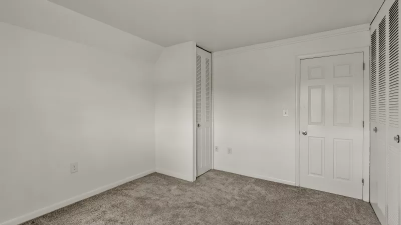 Bright bedroom at Rosedale Apartments with neutral walls, plush carpet, closet space, and natural window light