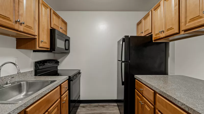 Updated kitchen at Rosedale Apartments with wood cabinets, granite countertops, black appliances, and wood-style flooring