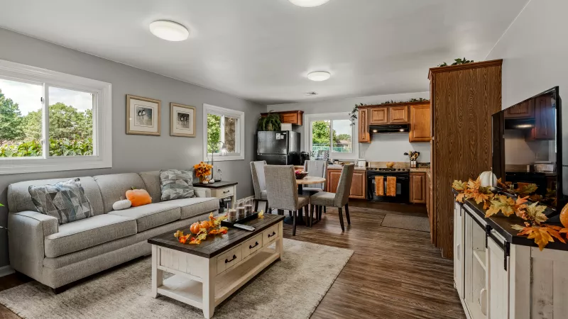 Spacious living room at Rosedale Apartments featuring modern gray sofa, dining area, and open kitchen with wood cabinetry and stainless-steel appliances