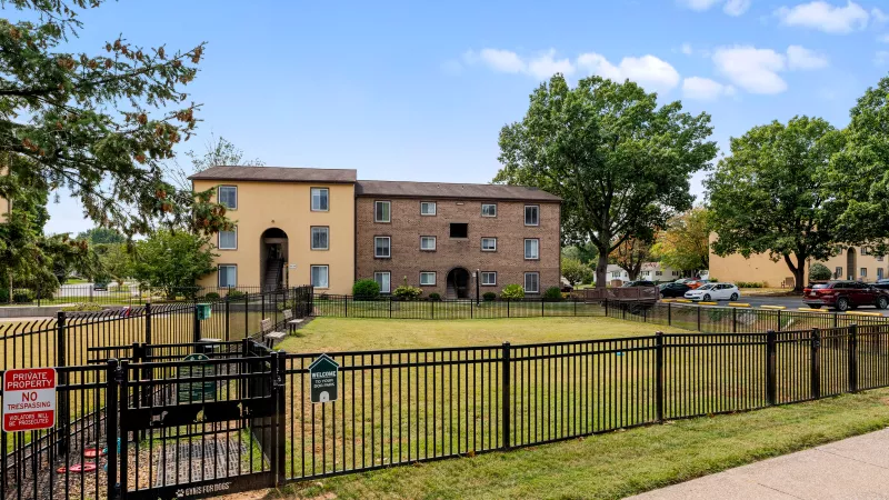 Fenced dog park at Rosedale Apartments with green space, benches, and pet waste station for residents and their pets