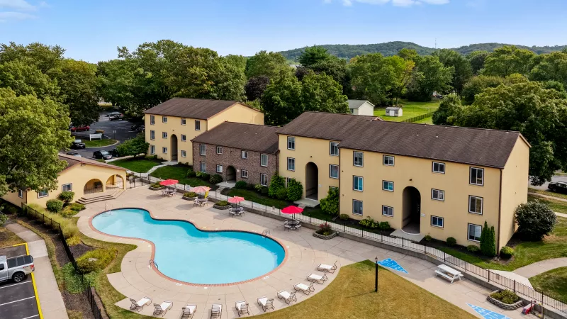 Large outdoor pool at Rosedale Apartments surrounded by sun loungers, shaded tables with umbrellas, and landscaped green space