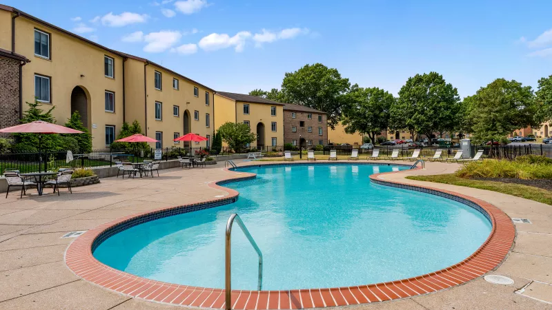 Resort-style swimming pool at Rosedale Apartments with lounge chairs, red umbrellas, and spacious sundeck for residents