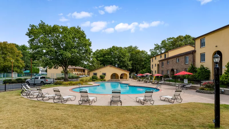 Sparkling swimming pool at Rosedale Apartments with lounge chairs, red umbrellas, and landscaped sundeck.