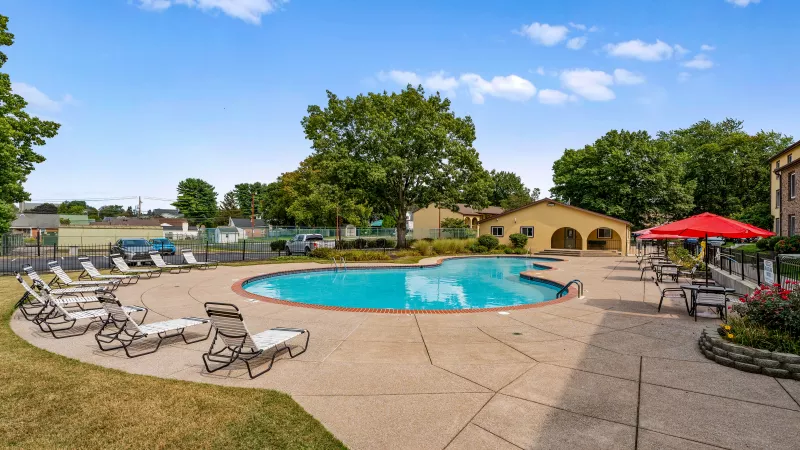 Resort-style swimming pool at Rosedale Apartments with lounge chairs, red umbrellas, and spacious sundeck surrounded by landscaped grounds.