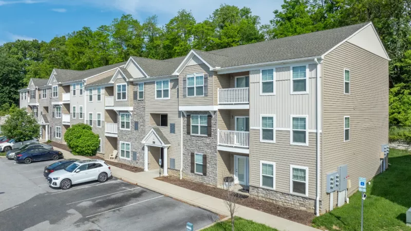 Wyndham Pointe Apartments three-story residential building with stone and beige siding, landscaped entrance, and adjacent parking area under clear blue sky.