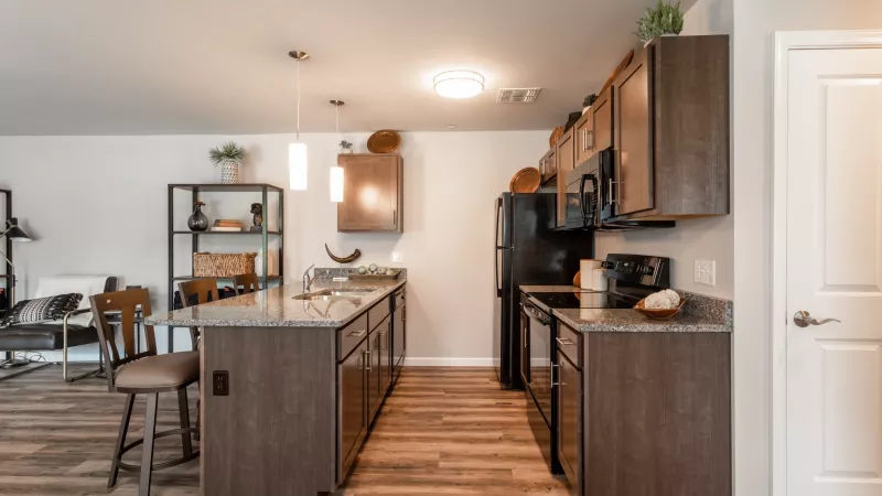 Modern kitchen at Wyndham Pointe Apartments with granite countertops, wood cabinetry, island seating, and stainless-steel sink.