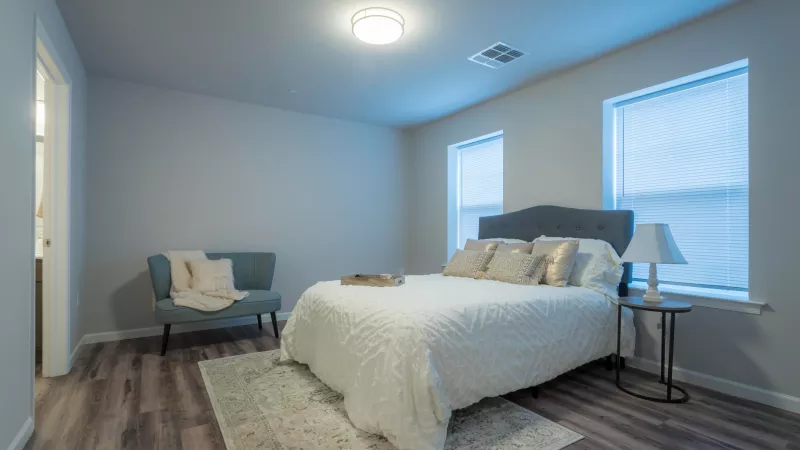 Primary bedroom at Wyndham Pointe Apartments featuring queen bed, plush bedding, soft lighting, and two windows for natural light.
