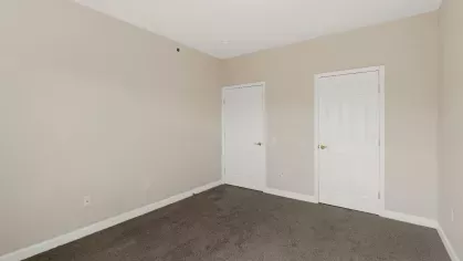 Empty bedroom with beige walls, carpet flooring, and two white closet doors.