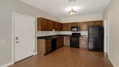 Kitchen with wood cabinetry, black appliances, L-shaped counter space, and wood-look flooring.