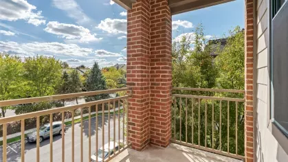 Private balcony with brick pillars and metal railing overlooking trees and parked cars on the street below.