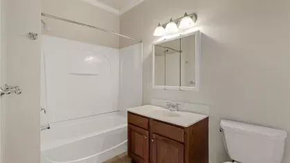 Bathroom featuring a wood vanity with storage, white countertop, toilet, and fiberglass shower surround with a curved shower rod.