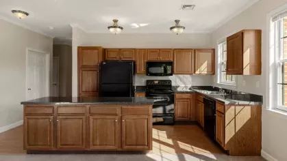 Kitchen with wood cabinets, black appliances, center island, and large windows providing natural light.