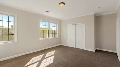 Spacious bedroom with neutral walls, carpet flooring, two windows, and double closet doors.
