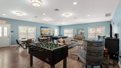 Community clubhouse game room with foosball table, seating areas, pool table, and large windows.
