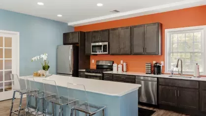 Clubhouse kitchen with stainless steel appliances, dark cabinets, orange accent wall, and island seating.