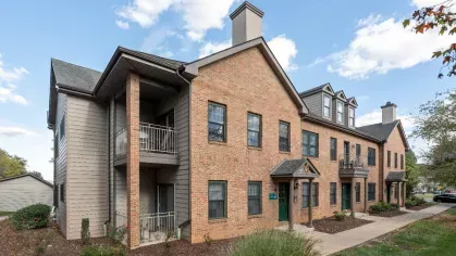 Two-story apartment building with brick and siding exterior, private balconies, and landscaped garden beds.