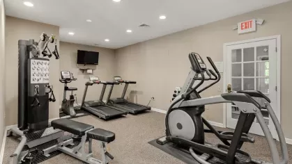 Fitness center with treadmills, stationary bikes, weight bench, and cable machine, plus mounted TV.