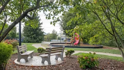 Outdoor seating area with two benches surrounded by trees and landscaping near a playground.