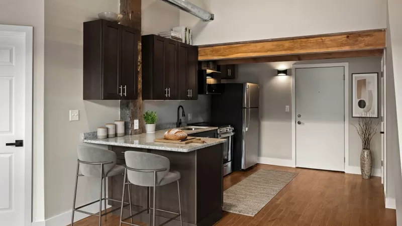 An entryway view showing the kitchen's breakfast bar with stone countertops and sleek grey barstools. The area features hardwood-style flooring and an accent of original timber framing.