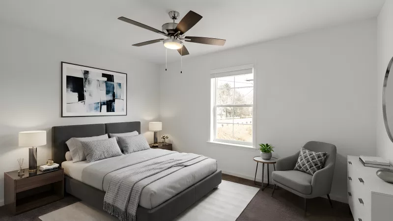 A second bedroom featuring a large window, neutral tones, and a dark grey upholstered bed frame. A ceiling fan and minimalist artwork complete the space.