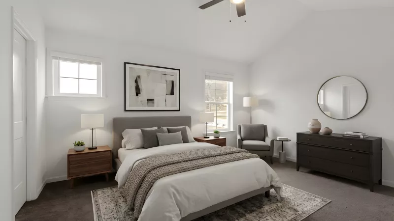 A spacious primary bedroom with neutral carpeting, white walls, and a large window. The room is styled with a tray ceiling and a modern ceiling fan.