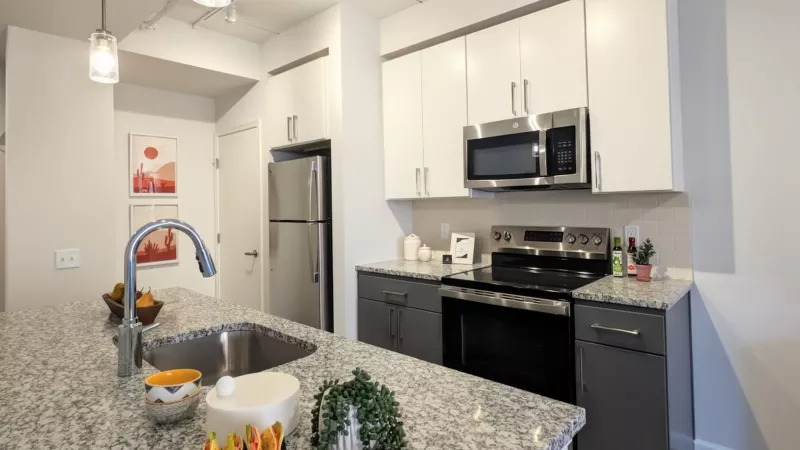 A modern kitchen featuring white upper cabinets, gray lower cabinets, stainless steel appliances, and a tiled backsplash behind the range.