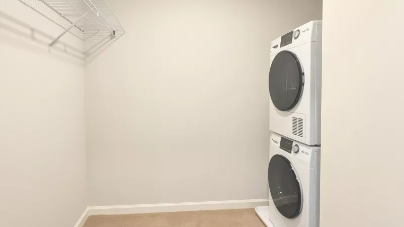 A laundry closet featuring a white stacked washer and dryer set, neutral carpeting, and a wire storage shelf above.