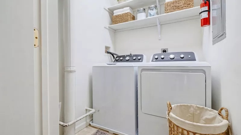 A dedicated laundry room featuring a white top-loading washer and dryer set, built-in storage shelving, and tile flooring.