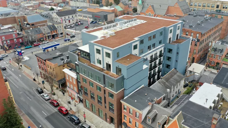 Aerial photograph shows a modern blue and white building contrasting with older brick structures along a city street.
