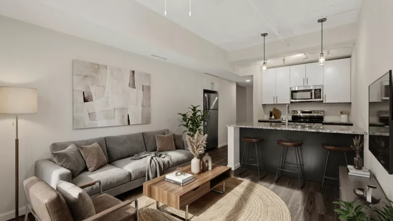 Photograph of a modern open-concept living room with grey sofa, armchairs, and a kitchen with white cabinets and dark island.