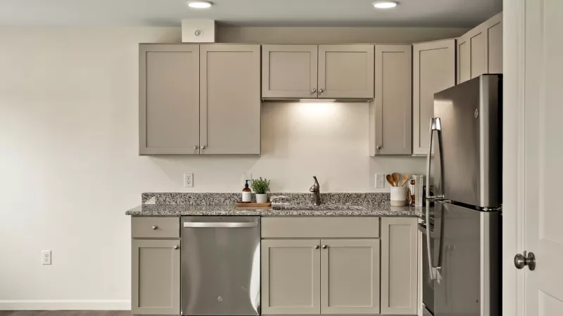 Modern kitchen with light gray cabinets, stainless steel appliances, speckled granite countertops, and dark wood floor.