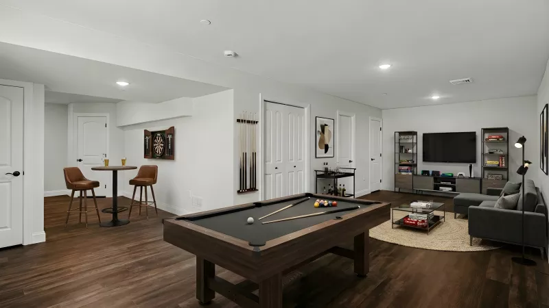 Modern basement rec room with a pool table, dark wood floors, gray sofa, TV, and a small bar table.