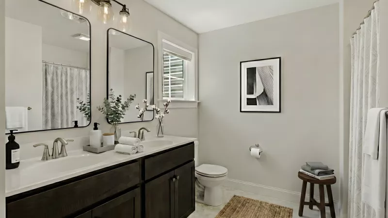 Bright, modern bathroom featuring a dark wood double vanity, two framed mirrors, toilet, and light beige walls.