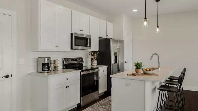 Bright kitchen features white cabinetry, stainless appliances, and an island with a sink and dark stools.