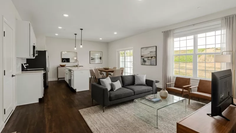 Spacious open-concept living, dining, and kitchen area featuring white cabinets, a gray sofa, and two brown leather chairs.