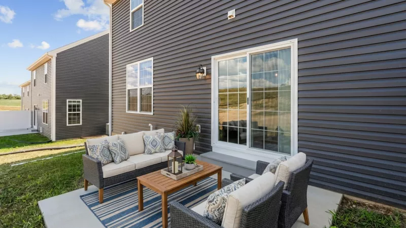Outdoor patio with dark gray house, sliding door, wicker sofa, chairs, wooden coffee table, and blue rug.