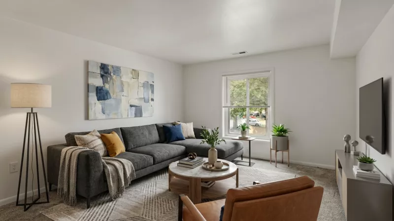 Bright, modern living room with a gray sectional sofa, brown leather armchair, coffee table, abstract art, and TV.