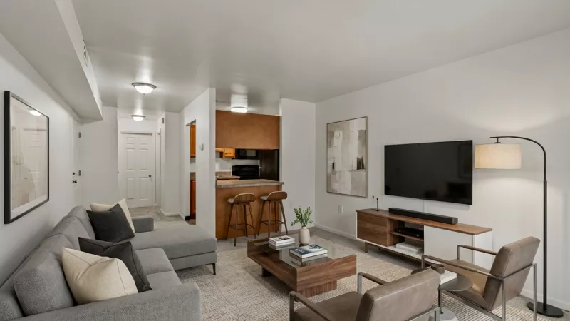 Photograph: Contemporary living room with gray sofa, TV, coffee table, and kitchen bar with two stools.