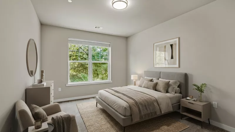 Modern bedroom with a bed, nightstand, dresser, armchair, and large window overlooking trees. Neutral tones.