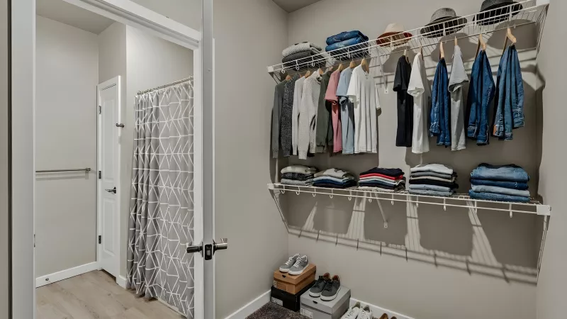 Organized walk-in closet with clothes on racks and folded on shelves, hats on top, and shoes on the floor.