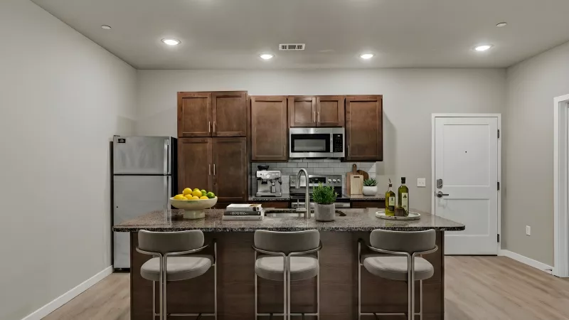 Modern kitchen with dark wood cabinets, stainless steel appliances, and a large island with three bar stools.