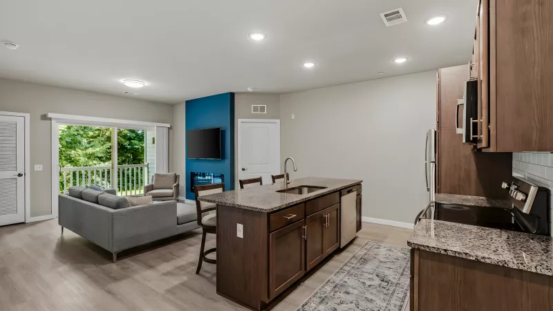 Open-concept living room with a grey sofa, blue accent wall with TV, and kitchen island with granite counters.