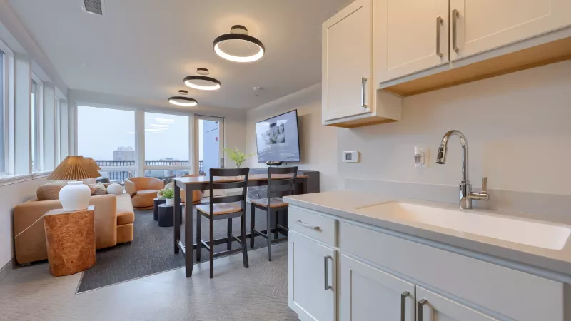 Bright, modern open-plan lounge with white kitchen cabinets, a high-top table, and a living area with a sofa and city views.