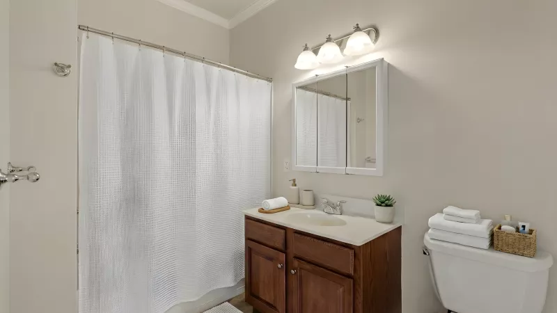 Clean bathroom with a white shower curtain, dark wood vanity, mirrored cabinet, and a toilet with stacked white towels.