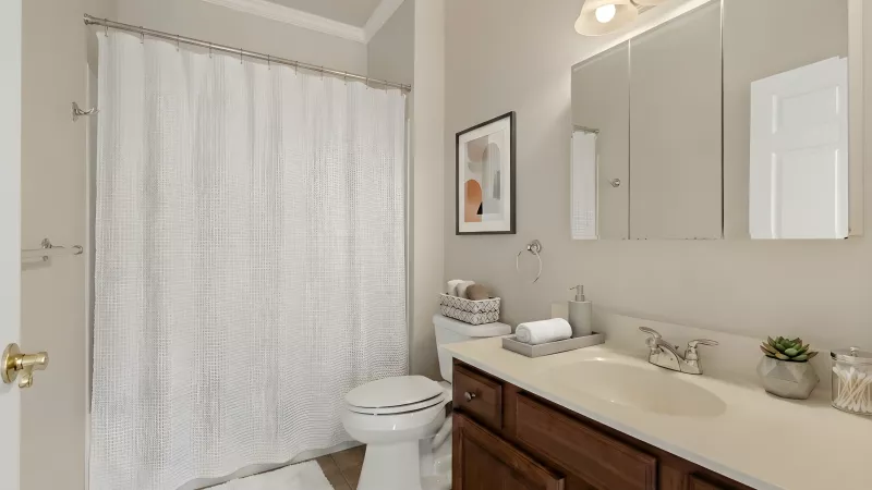 Clean, modern bathroom with a white shower curtain, toilet, dark wood vanity with sink, mirror, and light fixture.
