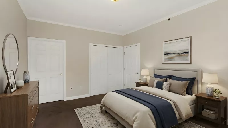 Well-lit modern bedroom with a bed, two nightstands, a dresser, and white doors. Beige walls, dark floor, blue and beige bedding.