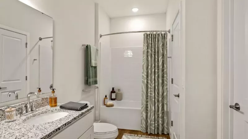 Modern bathroom with white walls, granite vanity, sink, mirror, toilet, bathtub, and green patterned shower curtain.