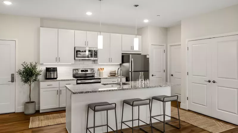 Modern kitchen with white cabinets, dark appliances, a granite island with three bar stools, and wood floors.