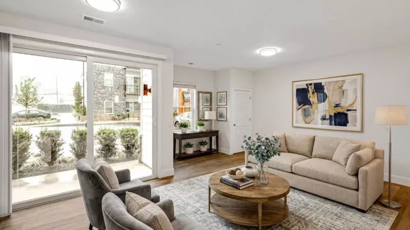 Bright living room with a beige sofa, two grey armchairs, a patterned rug, and a sliding glass door to an outdoor patio.
